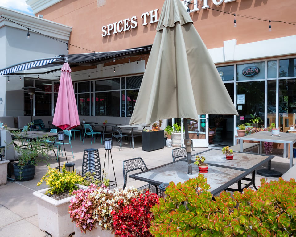 Outdoor patio of Spices Thai restaurant with tables, umbrellas, and colorful potted plants.