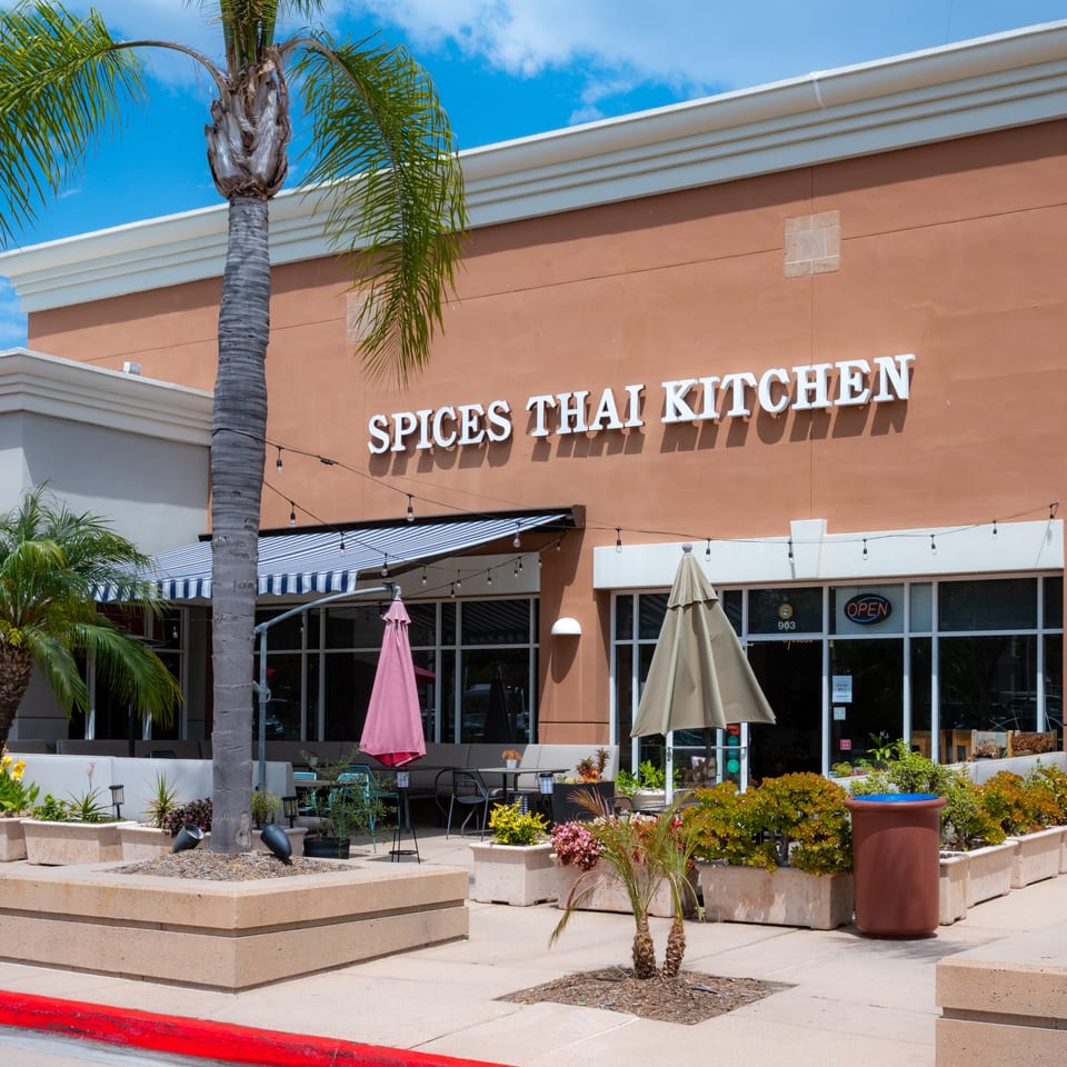 Exterior of Spices Thai Kitchen with outdoor seating, palm trees, and an "OPEN" sign.