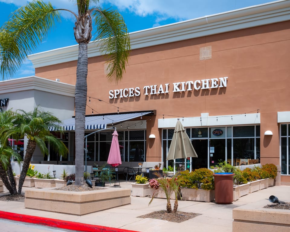 Exterior of Spices Thai Kitchen with outdoor seating, palm trees, and an "OPEN" sign.