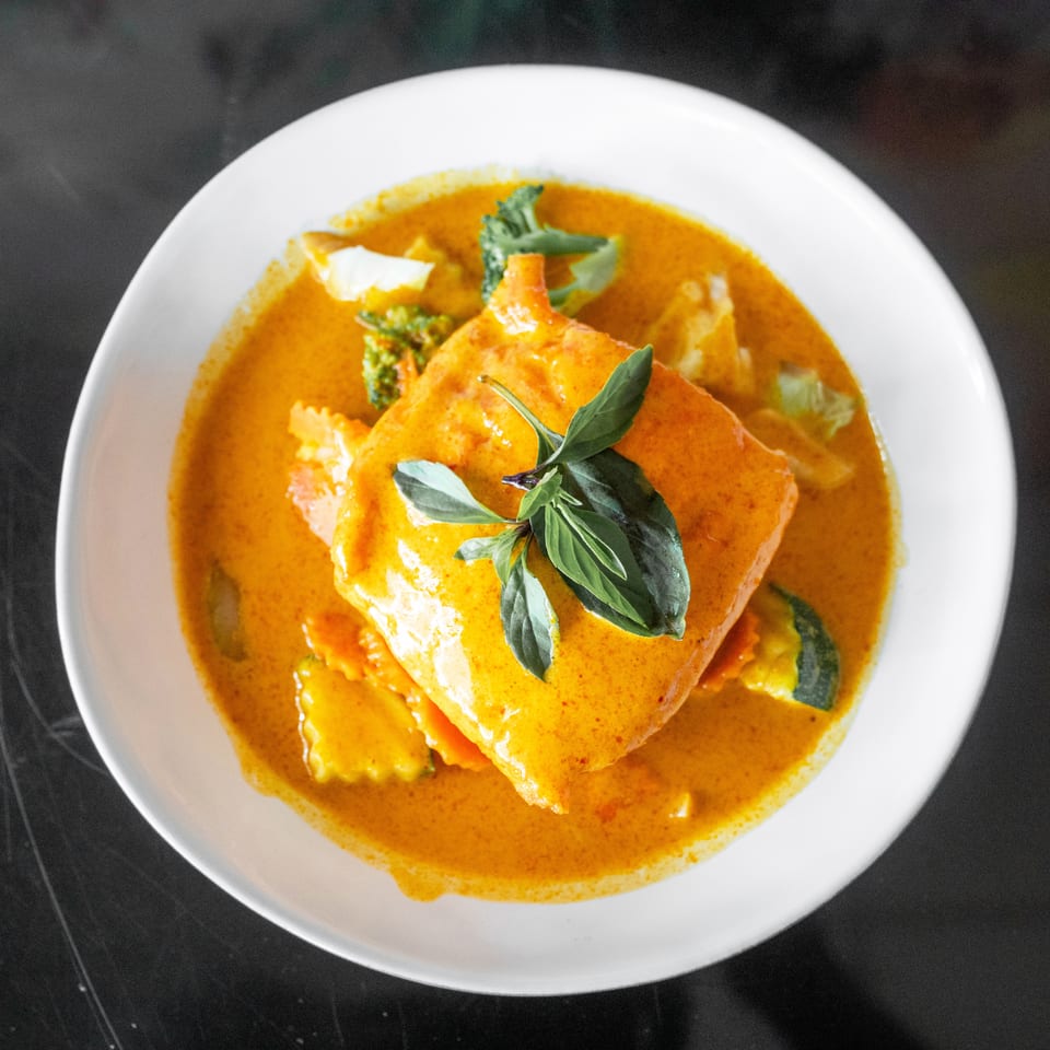 A vibrant red curry dish with a large piece of fish, garnished with fresh basil leaves.