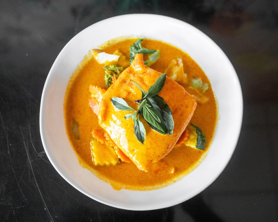 A vibrant red curry dish with a large piece of fish, garnished with fresh basil leaves.