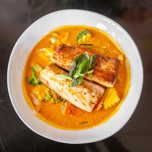 Two pieces of pan-seared fish in a red curry sauce with vegetables, garnished with basil.