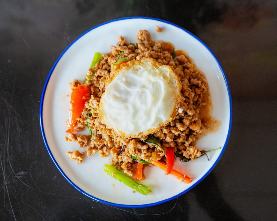 A plate of Thai basil chicken with a fried egg on top, garnished with red and green peppers.