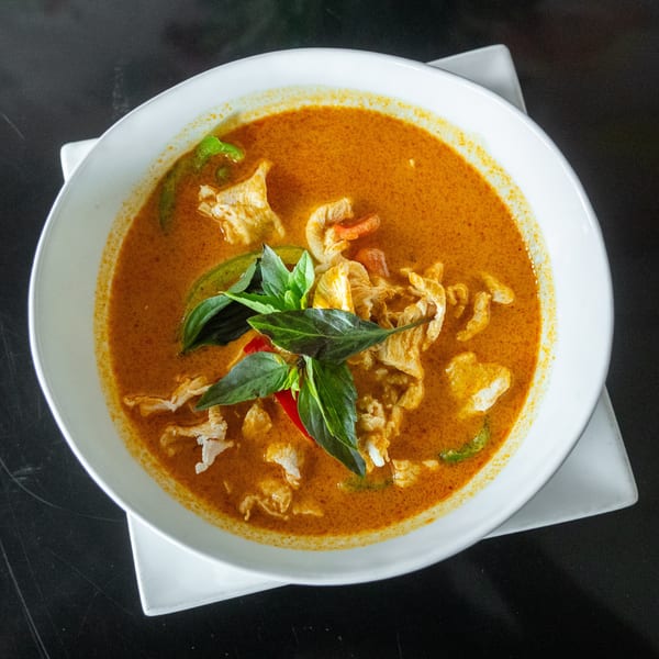 A white bowl filled with orange curry, chicken, green peppers, and basil leaves on a dark surface.