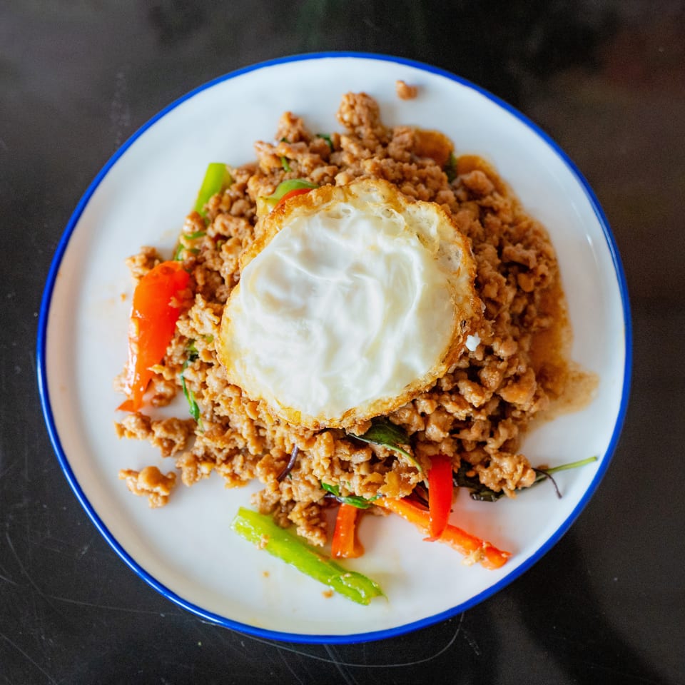 A plate of Thai basil chicken with a fried egg on top, garnished with red and green peppers.
