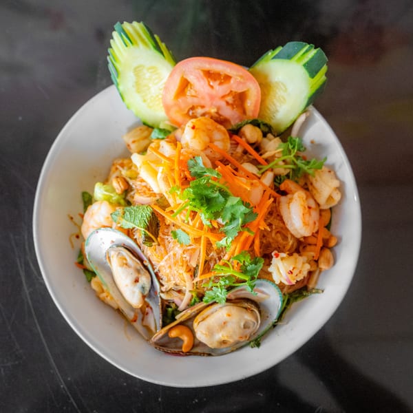 Spicy Thai glass noodle salad with shrimp, mussels, squid, and vegetables, garnished with cucumber and tomato.