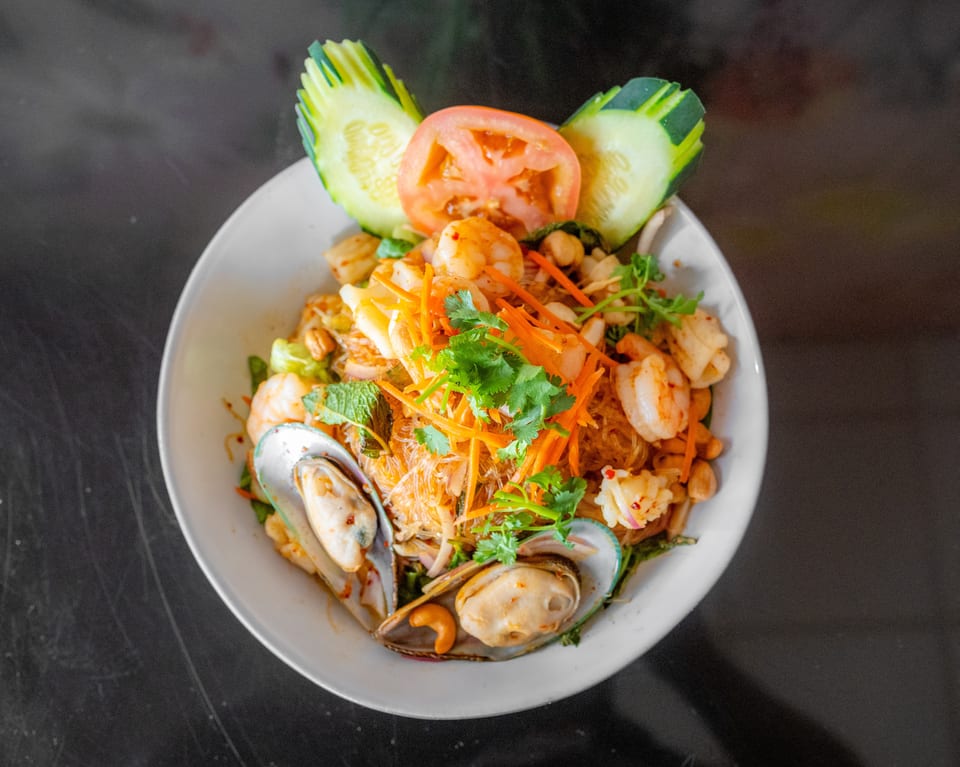 Spicy Thai glass noodle salad with shrimp, mussels, squid, and vegetables, garnished with cucumber and tomato.
