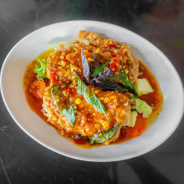 Crispy fried chicken or fish covered in a vibrant orange chili sauce with basil leaves and vegetables.