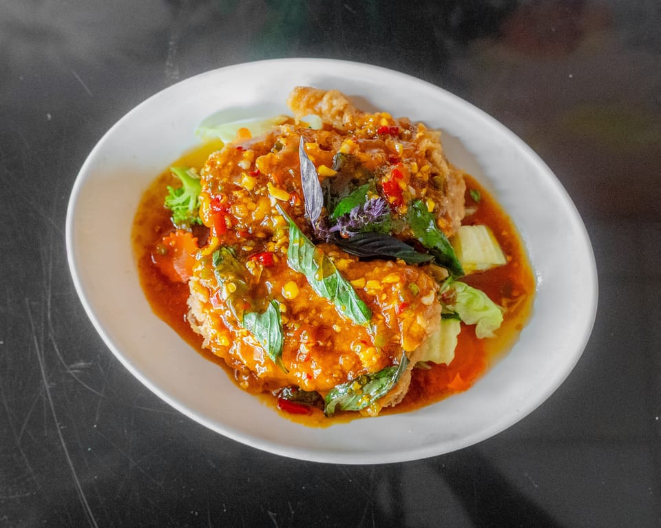 Crispy fried chicken or fish covered in a vibrant orange chili sauce with basil leaves and vegetables.