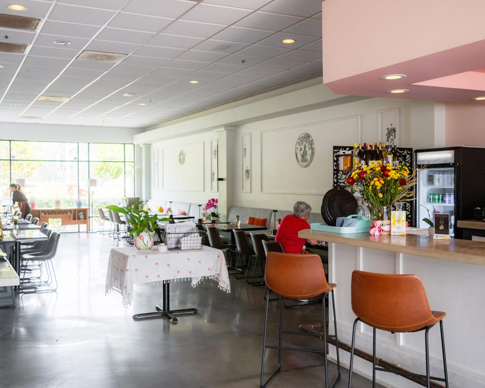 Bright, spacious restaurant interior with a bar, dining tables, and a large window overlooking trees.
