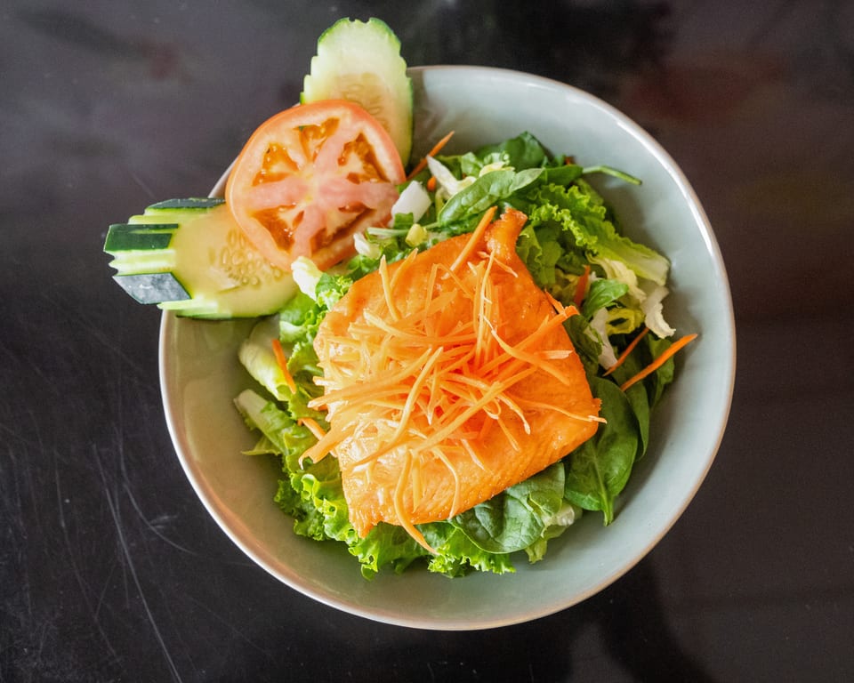 A fresh salad with mixed greens, a salmon fillet, shredded carrots, cucumber, and tomato slices.