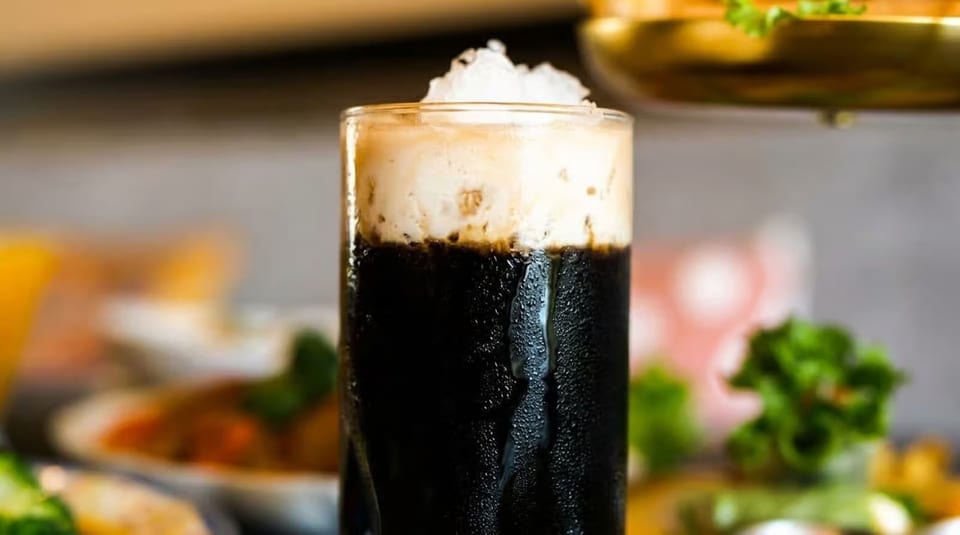 Close-up of a dark beverage with a thick layer of white foam and ice on top.
