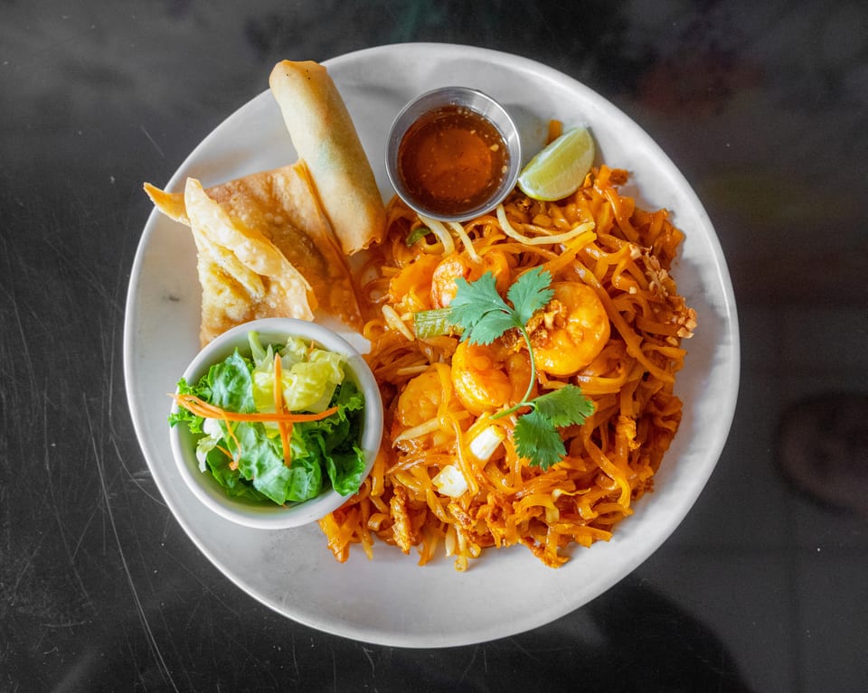 Pad Thai with shrimp, egg roll, fried wontons, side salad, and dipping sauce on a white plate.