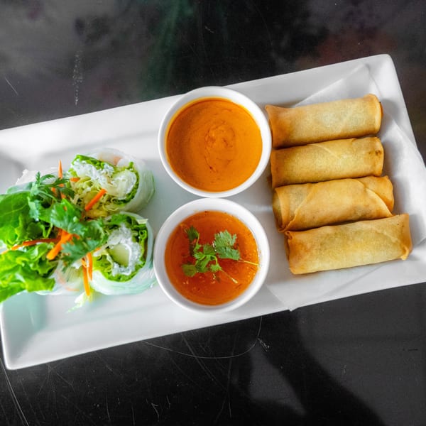 A white rectangular plate holds fresh spring rolls, fried egg rolls, and two dipping sauces.